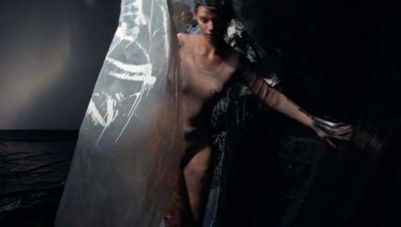 Katie O'Neill walking between two plastic sheets in a beige bodysuit.