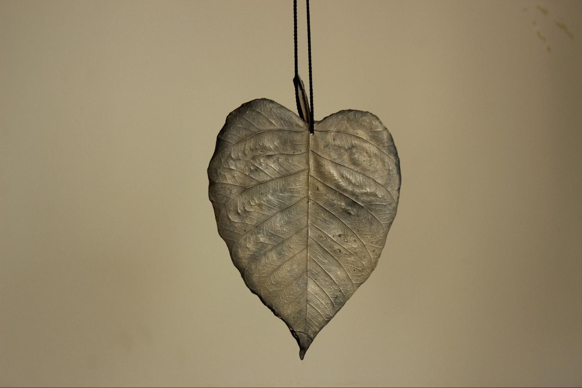 Bronze-coloured leaf-shaped jewellery with intricate vein and rib patterns on it, hanging from a string.
