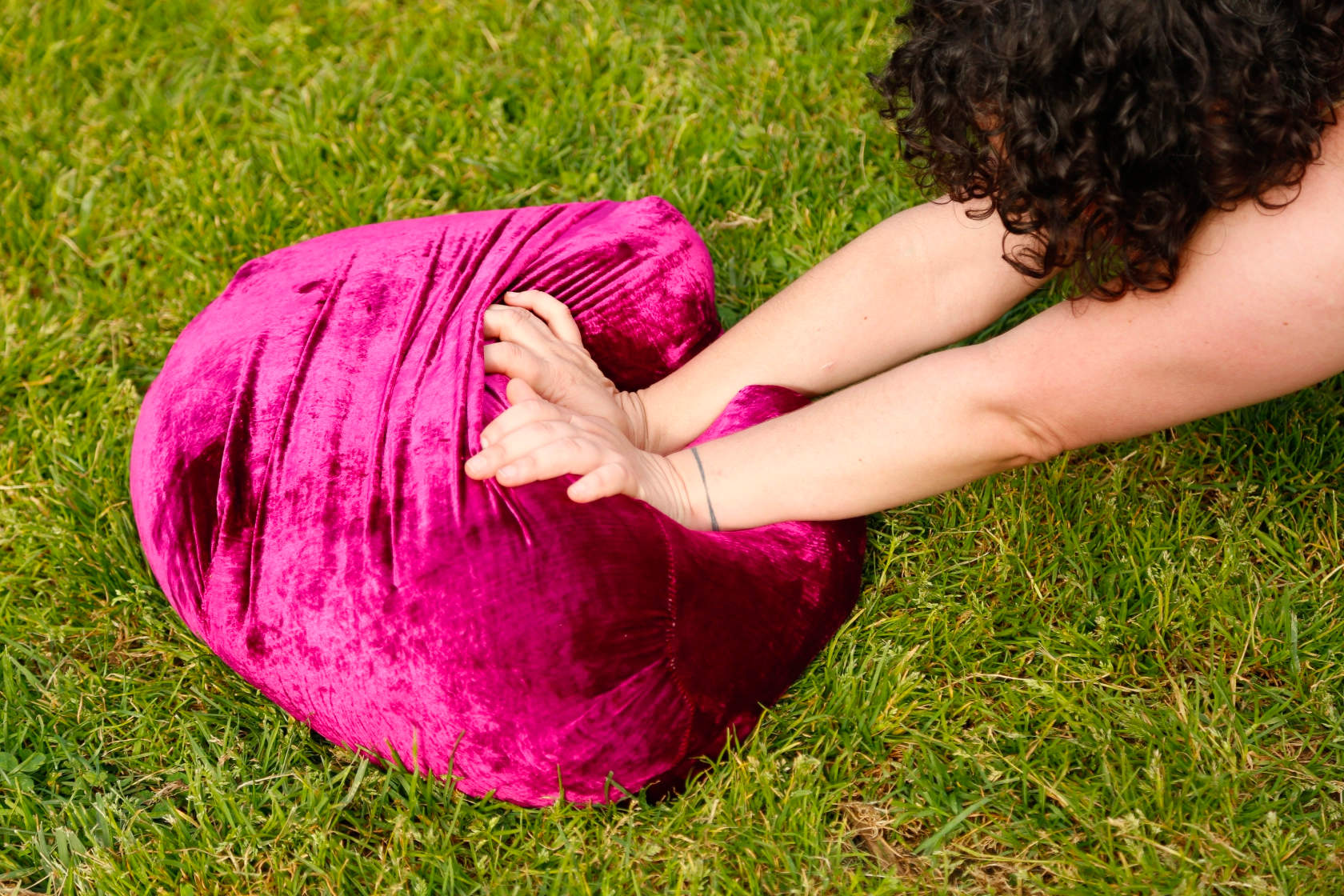 A person pushes a large, bright purple stuffed object in the grass.
